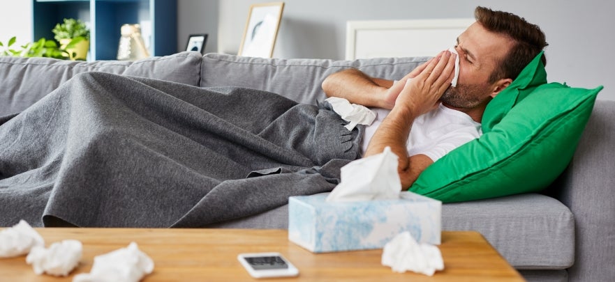 Sick man lying on sofa at home and blowing nose